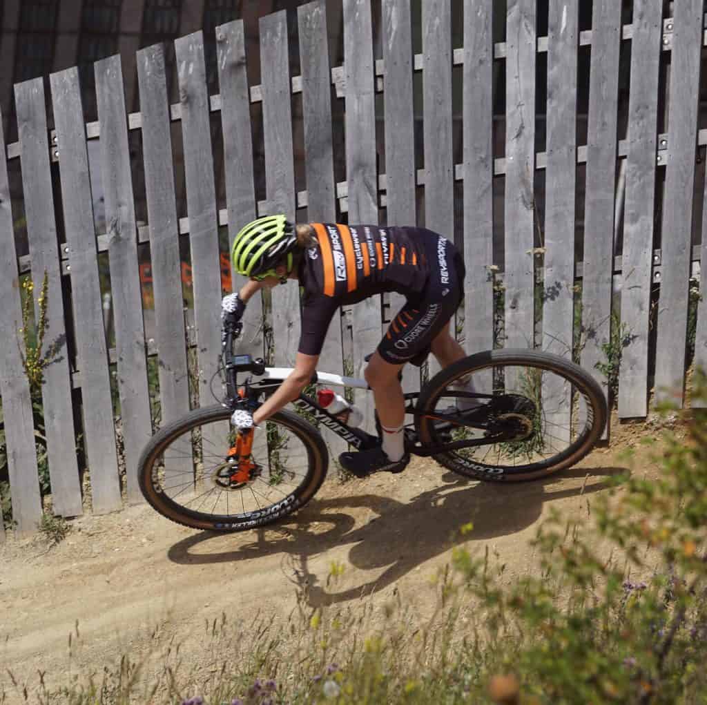 1. Een mountainbiker rijdt op een dirt trail met houten hekwerk op de achtergrond.